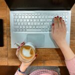 a person typing on a laptop with a cup of coffee